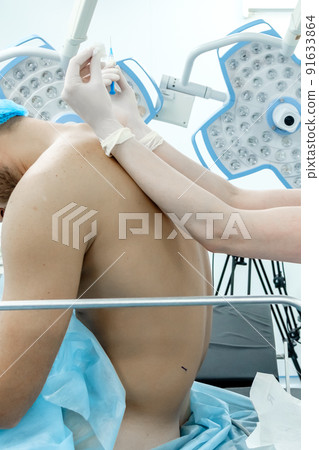 An anesthetist in white medical clothes, a mask and sterile gloves holds a needle in his hands. An anesthetist in white medical clothes, a mask and sterile gloves holds a needle in his hands. 91633864