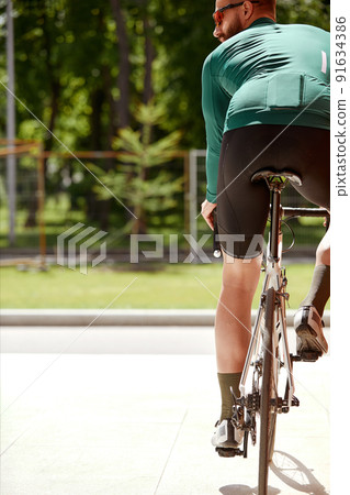 The young man rides a bicycle along around the city. Photo from the back. Outdoor vacation concept. The young man rides a bicycle along around the city. Photo from the back. Outdoor vacation concept. 91634386