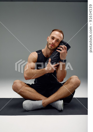 Athletic man using a foam roller to relieve sore muscles after a workout. 91634539