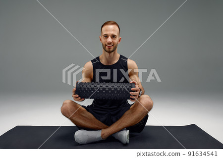 Athletic man using a foam roller to relieve sore muscles after a workout. 91634541