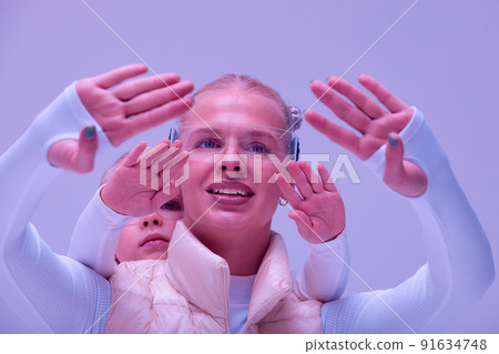 Woman with little girl in futuristic costume wearing smart led glasses of virtual reality while touching air. Augmented reality game, future technology, AI concept. VR. Neon light. 91634748