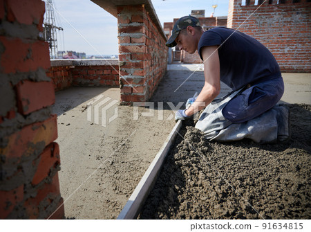 Side view of young worker in protective gloves leveling concrete slab using trowel on fresh air. Concept of process working with cement and special equipments in good weather. Side view of young worker in protective gloves leveling concrete slab using trowel on fresh air. Concept of process working with cement and special equipments in good weather. 91634815