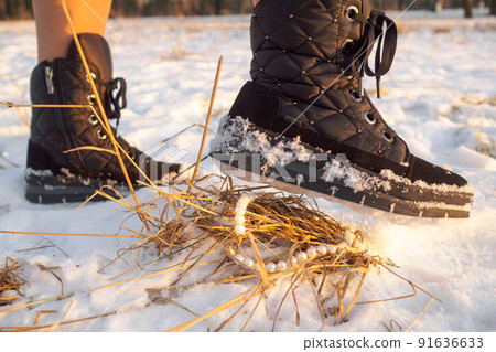 A foot in a winter black boot with adhering snow hangs over the pearl jewelry. A foot in a winter black boot with adhering snow hangs over the pearl jewelry. 91636633
