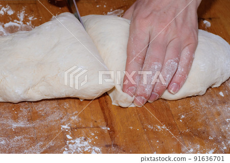 Female hands cut with a knife a kneaded dough on a wooden table.  91636701