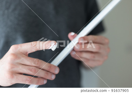 Man putting glue by finger on decorative plastic corner for the wall protection in apartment.  91637905