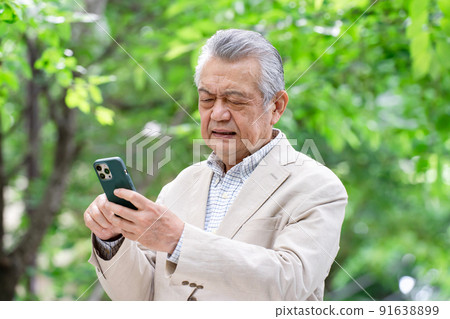 Senior man operating a smartphone with a troubled face 91638899