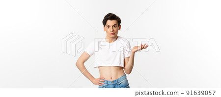 Handsome androgynous man in crop top looking confused, shrugging clueless, standing over white background 91639057