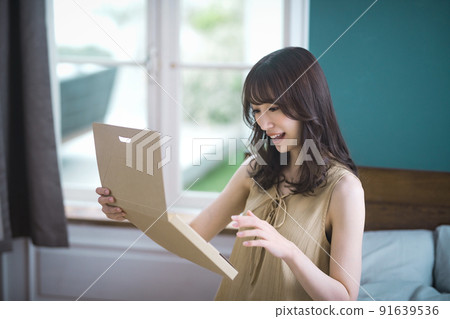 Lifestyle image of a young woman checking mail-order luggage in the room 91639536