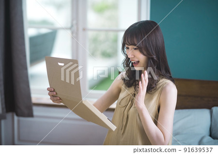 Lifestyle image of a young woman checking mail-order luggage in the room 91639537
