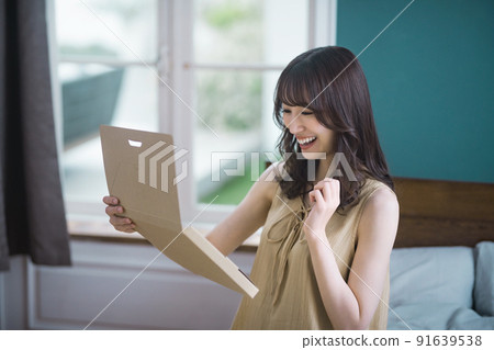Lifestyle image of a young woman checking mail-order luggage in the room 91639538
