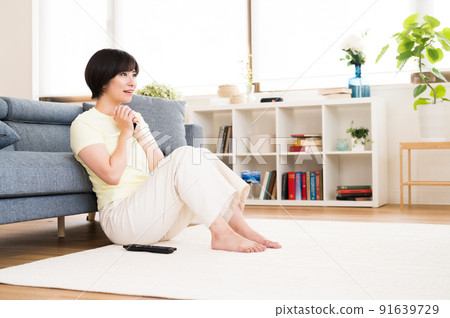 A woman watching TV with a smartphone in one hand A woman watching TV with a smartphone in one hand 91639729