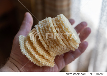 Male holding prepared waffle crusts in his hand. Stack of crispy hexagonal crusts to be stuffed with ground meat and other fillings. Home cooking. Selective focus. 91640286