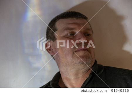 A portrait of a quiet, serious man. Unshaven man leaning tiredly against the wall. A middle-aged male with short graying brown hair. Looking away past the camera. Selective focus. Low key. 91640316