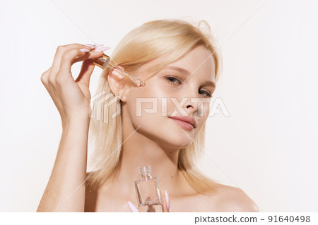Beautiful young girl with blond hair applying serum, oil on face isolated on white background. Concept of cosmetics, makeup, natural beauty Beautiful young girl with blond hair applying serum, oil on face isolated on white background. Concept of cosmetics, makeup, natural beauty 91640498