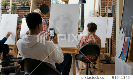 Creative student taking picture of vase sketch on smartphone in art class. Young man using mobile phone to take photo and remember drawing skills technique at educational lesson. 91641543