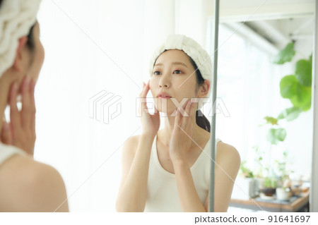 A woman checking the condition of her skin in front of a mirror 91641697