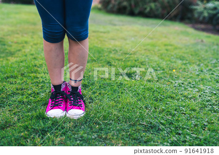 Girl in stylish pink sneakers standing on fresh green grass 91641918