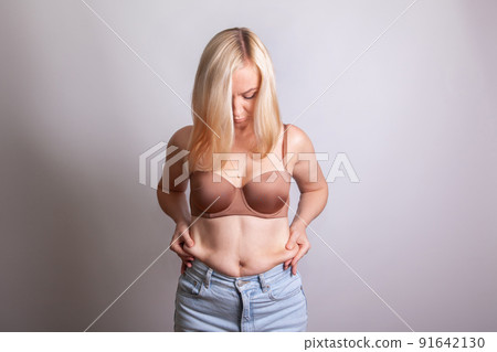 Woman with blonde hair squeezes belly fat on her stomach 91642130