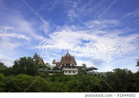 Thai temple is located on hillside surrounded by nature of forest and bright blue sky. Thai temple is located on hillside surrounded by nature of forest and bright blue sky. 91644002