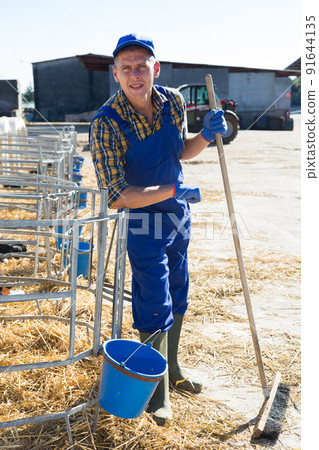 Smiling farmer standing near outdoors stall with calves Smiling farmer standing near outdoors stall with calves 91644135