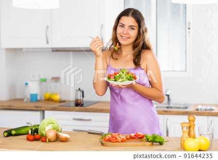 Portrait of positive woman in nightdress eating salad at home Portrait of positive woman in nightdress eating salad at home 91644235