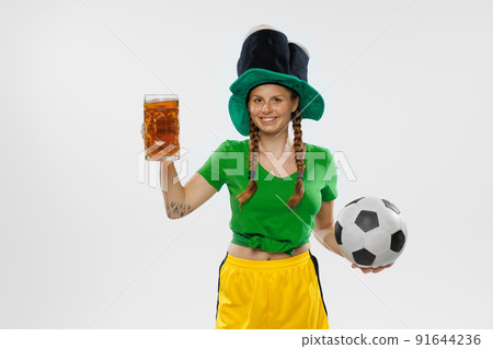 Happy excited woman in green yellow football kit holding beer mug and football ball supports favorite team. Soccer fans, competition, sport, oktoberfest concept 91644236