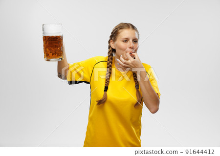 Young excited woman in yellow football kit holding beer mug and supports favorite team. Soccer fans, competition, sport, oktoberfest concept 91644412