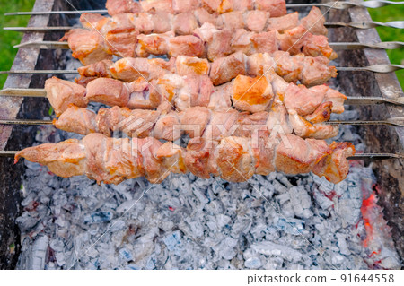 Juicy slices of pork meat are strung on skewers and grilled in charcoal grill. Juicy slices of pork meat are strung on skewers and grilled in charcoal grill. 91644558