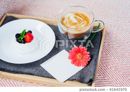 Cup of coffee, Pavlova dessert cake, gerbera flower and blank postcard with copy space on the tray with gray napkin. Breakfast for loved one. Romantic surprise. Take a break, relax. Selective focus. 91645970