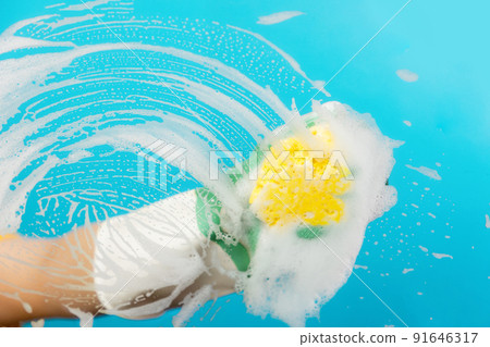 Female hand in rubber gloves wipes the glass with a yellow foam sponge. Light blue background. The concept of professional cleaning service Female hand in rubber gloves wipes the glass with a yellow foam sponge. Light blue background. The concept of professional cleaning service 91646317