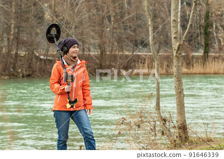 portrait of a girl with a metal detector on his shoulder, against the river and forest portrait of a girl with a metal detector on his shoulder, against the river and forest 91646339