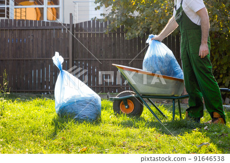 Man gardener puts bags of compost in the cart. Green uniform 91646538