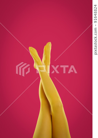 Woman wearing yellow tights on crimson background, closeup of legs 91648824