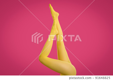 Woman wearing yellow tights on crimson background, closeup of legs 91648825