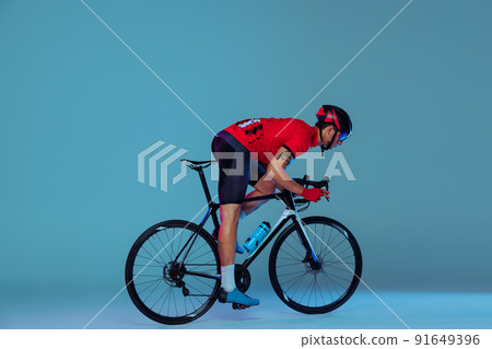 Studio shot of professional cyclist in red sports uniform, goggles and a helmet on a blue background. Concept of active life, rest, travel, energy, sport Studio shot of professional cyclist in red sports uniform, goggles and a helmet on a blue background. Concept of active life, rest, travel, energy, sport 91649396