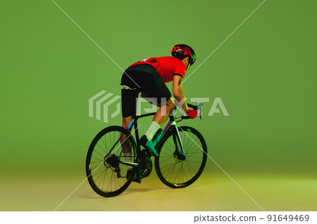 Young sportsman, cyclist on bicycle in sports uniform and protective helmet training isolated on green background. Concept of active life, rest, travel, energy, sport Young sportsman, cyclist on bicycle in sports uniform and protective helmet training isolated on green background. Concept of active life, rest, travel, energy, sport 91649469