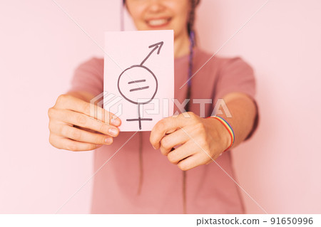 Girl holding paper with gender equality sign against pink background Girl holding paper with gender equality sign against pink background 91650996