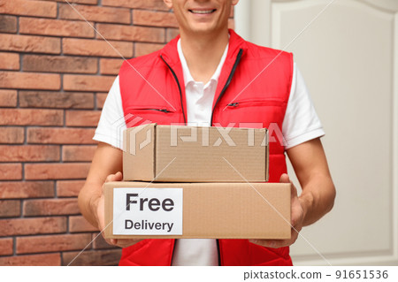 Courier holding parcels with sticker Free Delivery indoors, closeup Courier holding parcels with sticker Free Delivery indoors, closeup 91651536