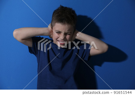 Scared little boy closing his ears near blue wall. Domestic violence concept 91651544