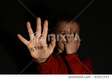 Abused little boy showing palm with word STOP against black background, focus on hand. 91651555