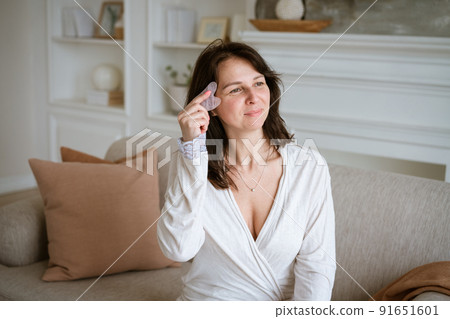 Shot of woman holding pink gouache scraper to massage her face during her 91651601