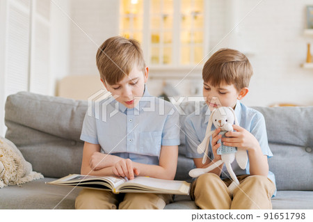 Boys are reading book while sitting on couch at home. Brothers read book. Older 91651798