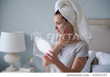 Nice woman with towel on her head applies moisturizing mask to her face 91652251