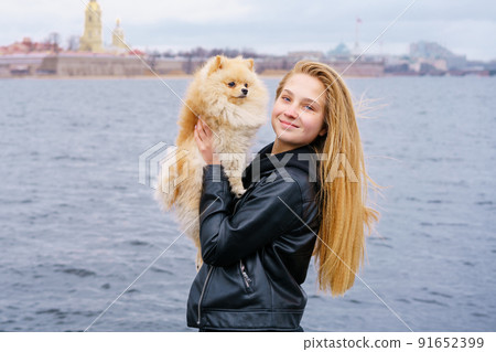 Young woman hugs spitz dog outdoors on embankment of city river in black Young woman hugs spitz dog outdoors on embankment of city river in black 91652399