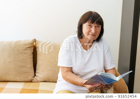 Portrait of attractive focused cheerful woman sitting on sofa reading book 91652454