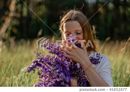 Close up portrait of young beautiful redhead woman with freckles, wearing white dress, posing in the nature. Girl with red hair holding flowers. Natural beauty. Diversity, individual uniqueness. 91652877