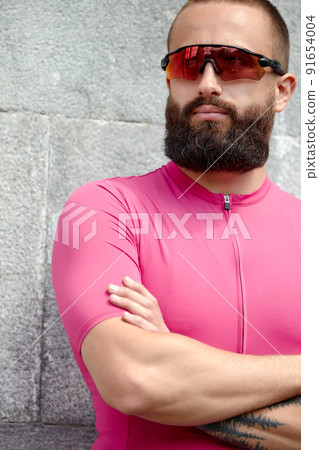 Portrait of sportsman in pink sportwear resting after an workout while standing against cement wall background with copy space area for text message or advertising, man runner taking break after run Portrait of sportsman in pink sportwear resting after an workout while standing against cement wall background with copy space area for text message or advertising, man runner taking break after run 91654004
