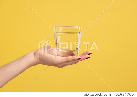 Close up woman hand holding glass with water on palm, advertising of fresh pure beverage, best way to restore water balance. Indoor studio shot isolated on yellow background. Close up woman hand holding glass with water on palm, advertising of fresh pure beverage, best way to restore water balance. Indoor studio shot isolated on yellow background. 91654769