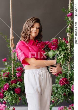 a brunette woman in white pants and a pink blouse with peonies and a swing. a brunette woman in white pants and a pink blouse with peonies and a swing. 91656436