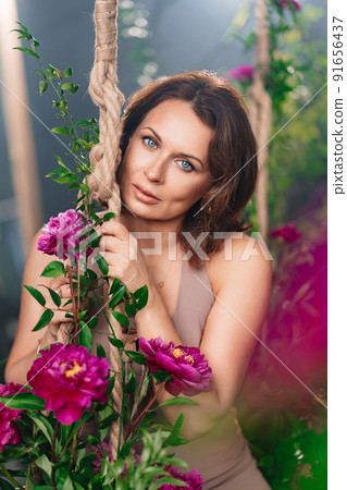 a pretty brunette woman on a swing with peony flowers. a pretty brunette woman on a swing with peony flowers. 91656437